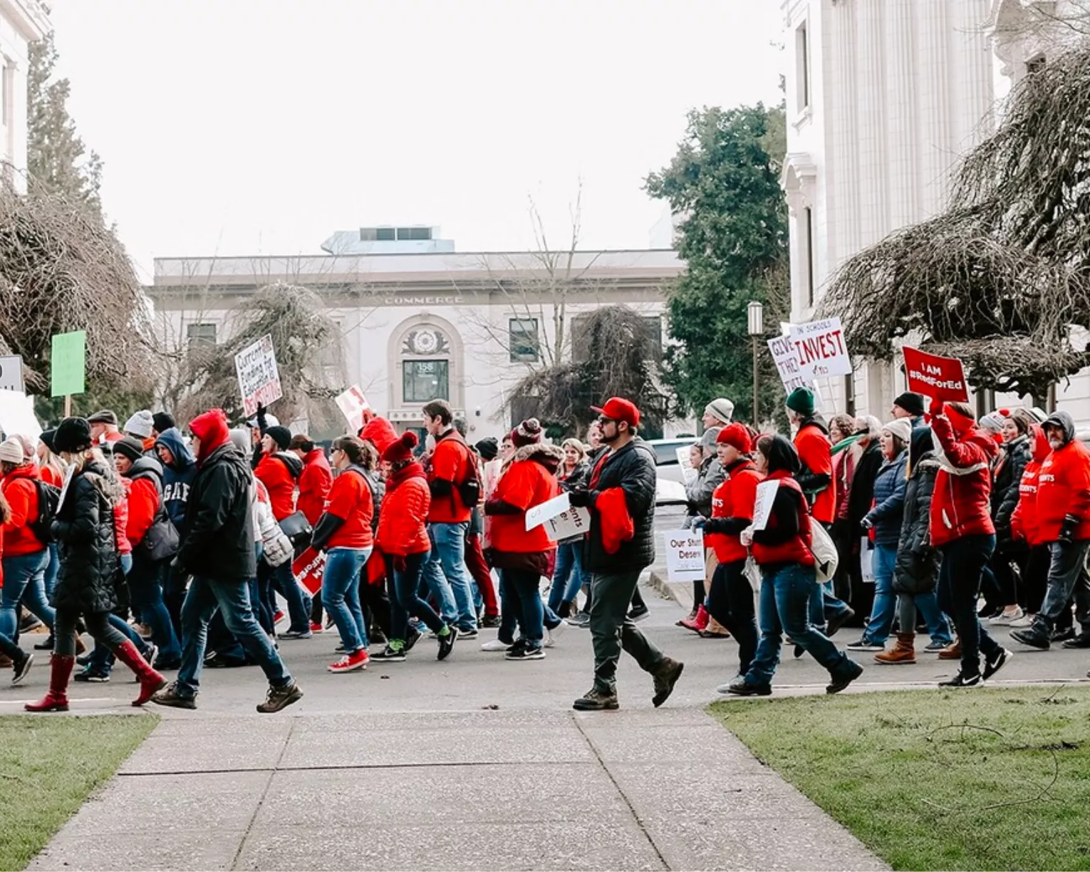Members march down the street wearing red and carrying signs.