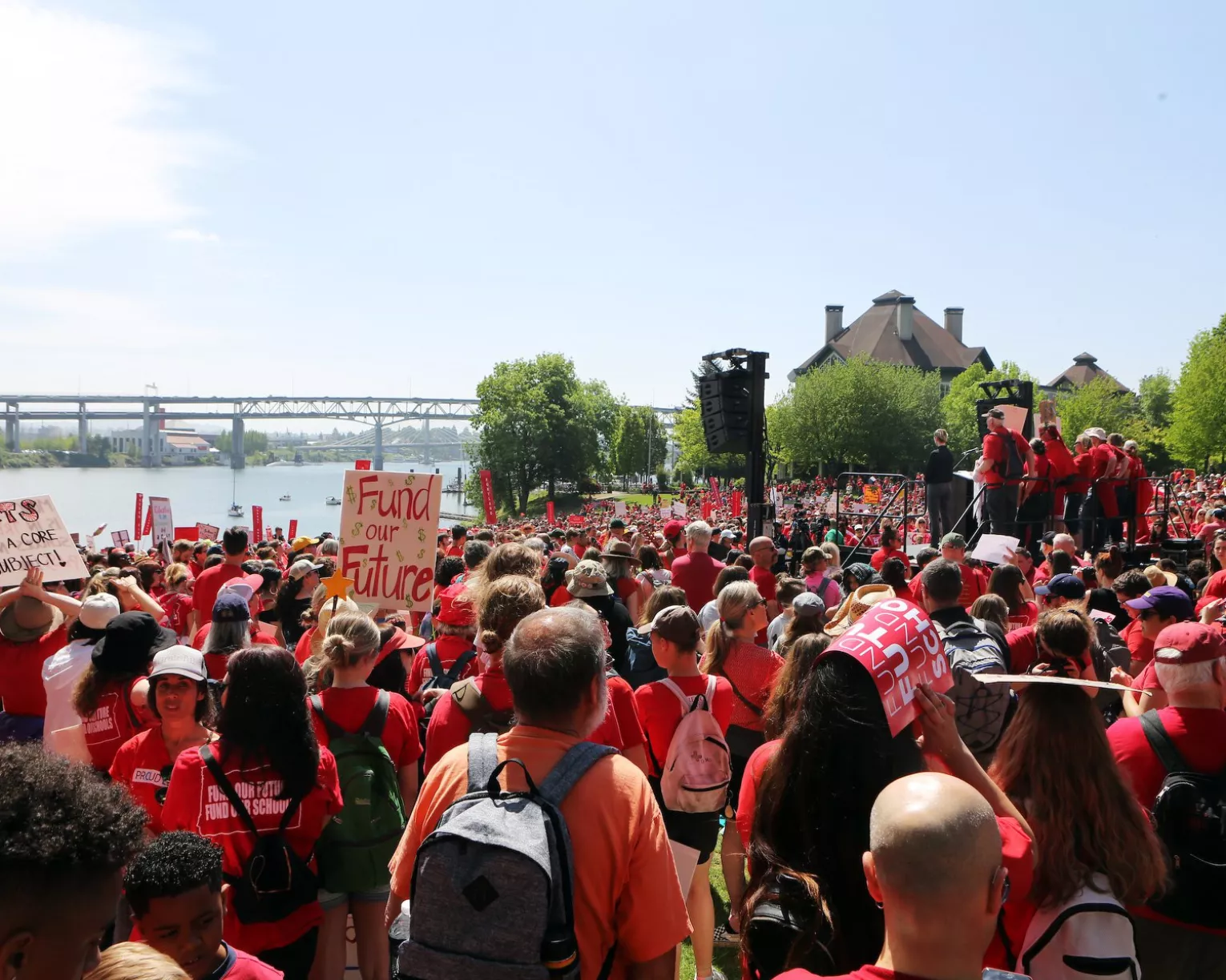 A crowd of members stand at a rally by a riverside all dressed in red, waiting for someone to speak to the crowd.