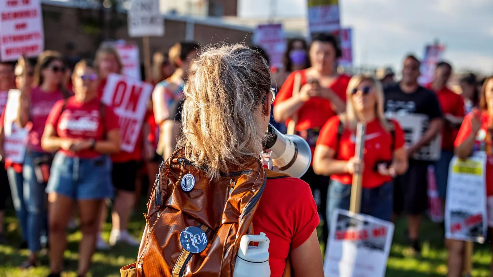 Educators rally with picket signs. One educator, standing in the front of the group, holds a bullhorn.
