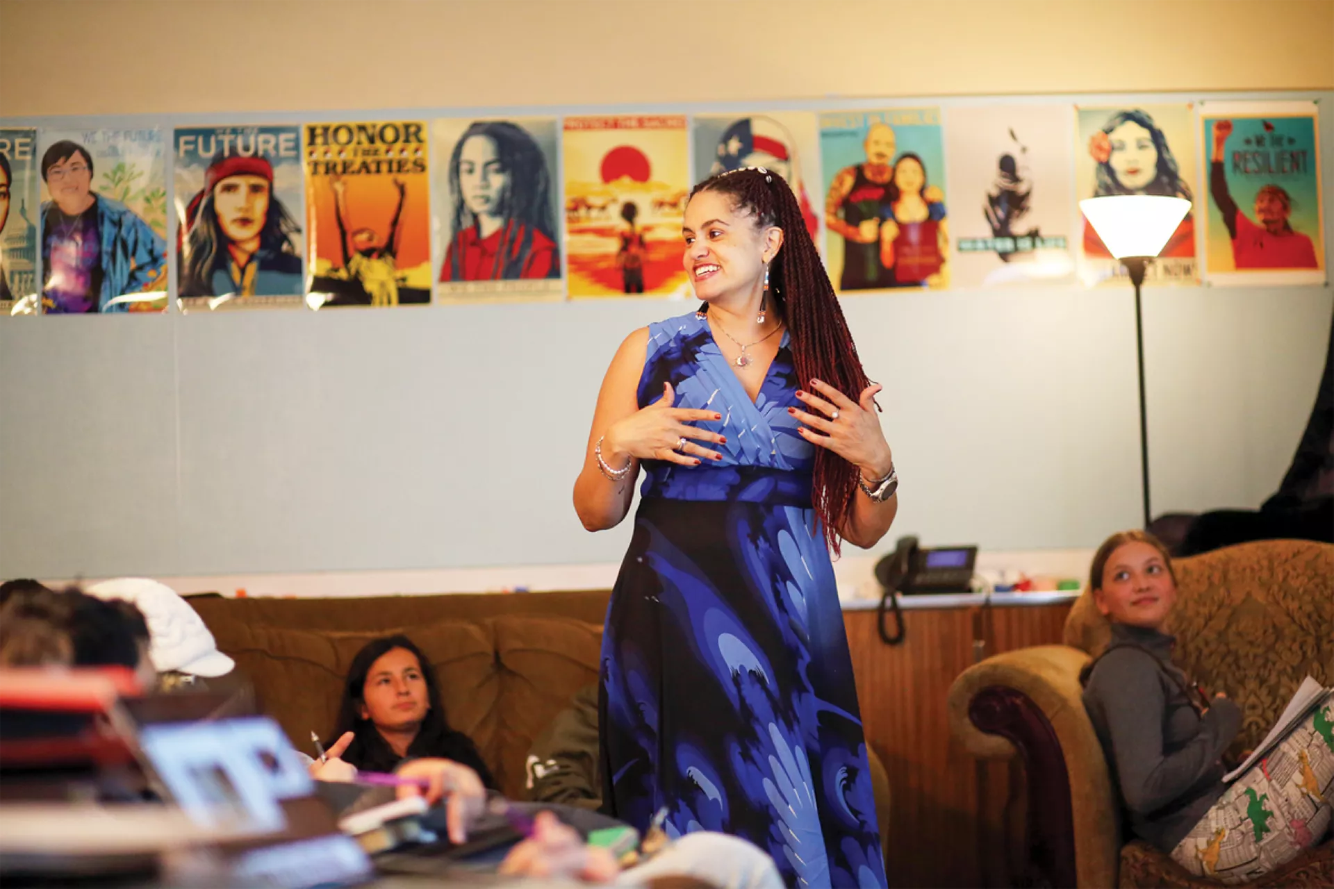 Educator Katherine Watkins stands in a classroom with students spread out in various chairs and couches reading.