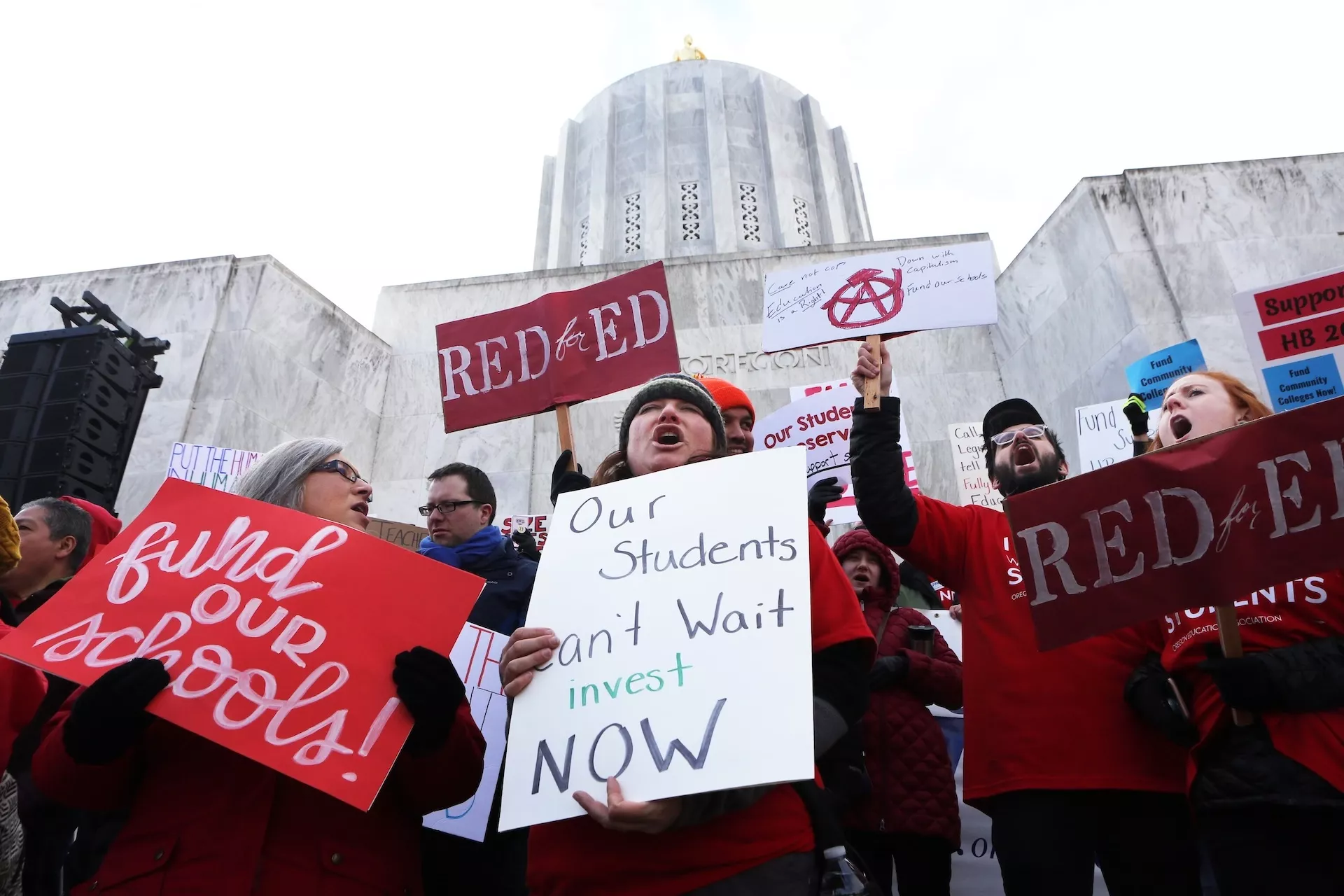 educators wearing red rally and hold signs in from of the state capitol in Salem, Oregon