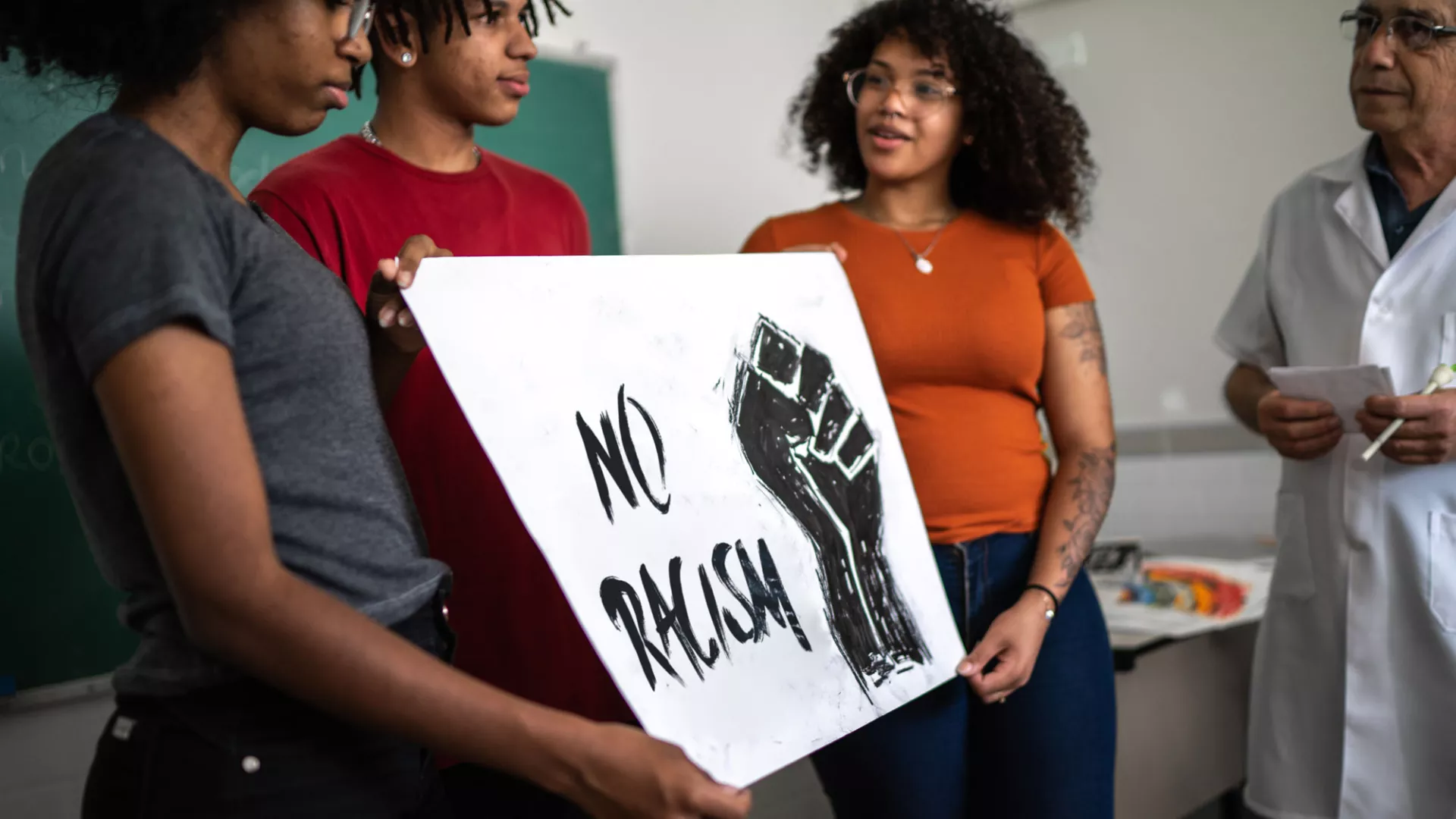 three black students hold a sign that says no racism