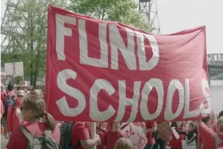 Educators march with a large red banner that reads "Fund Schools"