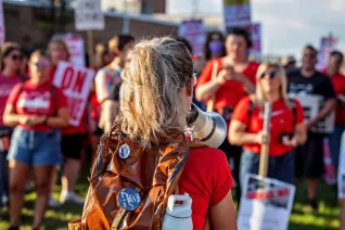 Educators rally with picket signs. One educator, standing in the front of the group, holds a bullhorn.