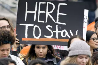 activists protesting immigration policy with sign that says Here to Stay