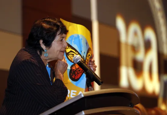 Dolores Huerta speaking at dais, NEA butterfly poster in background