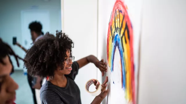A student tapes a poster to the wall. The poster contains a rainbow with the word "love" written on it.