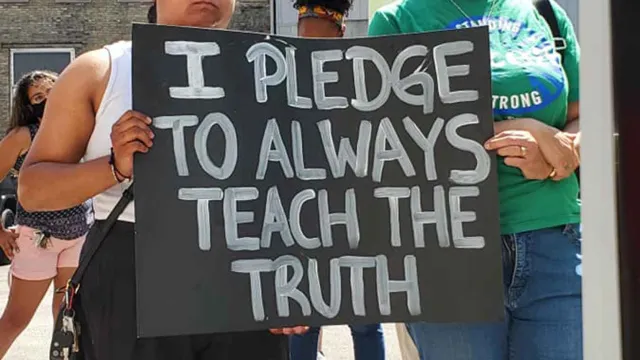 Two women carry a "I Pledge to Teach the Truth" poster at a march