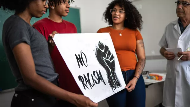 three black students hold a sign that says no racism