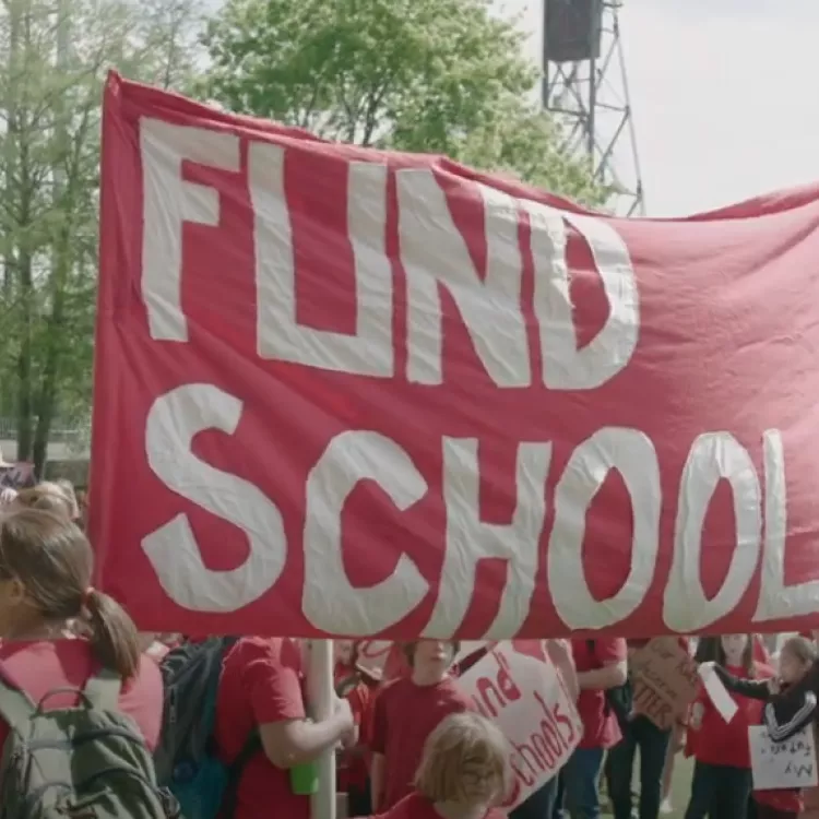 Educators march with a large red banner that reads "Fund Schools"
