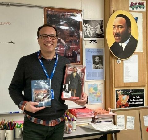 Kellen Akiyama stands in their classroom with some of their favorite equity resources.